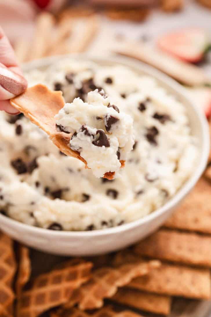 A hand lifting up a scoop of sweet cannoli dip on a piece of waffle cone.