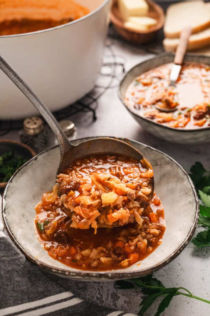 A ladle scooping stuffed cabbage roll soup into a rustic bowl.