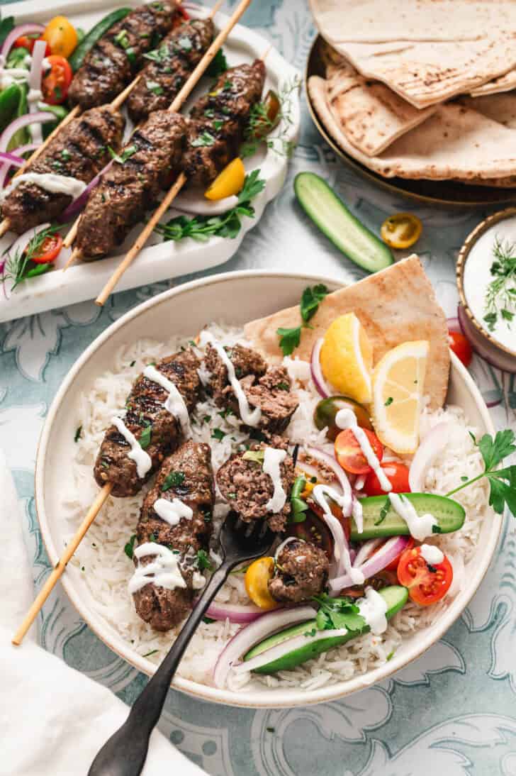 A bowl filled with rice, Lebanese kafta, vegetables, pita bread and drizzled with creamy sauce.