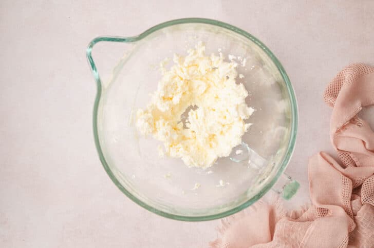 Soft cheese beaten in the glass bowl of a stand mixer.