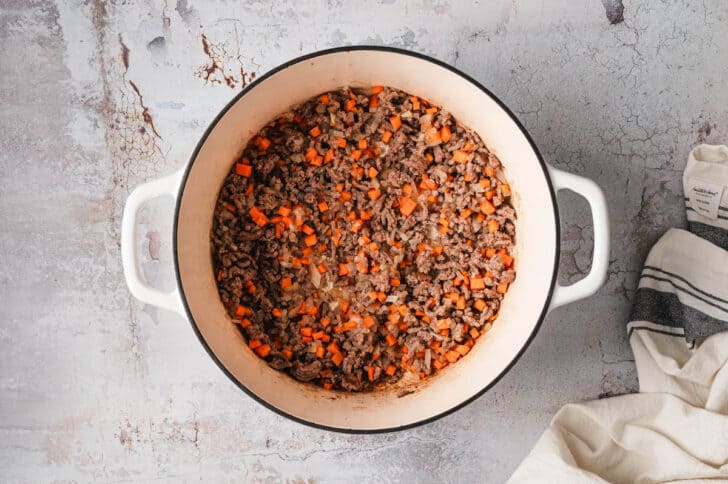 A white Dutch oven filled with cooked ground beef and carrot.