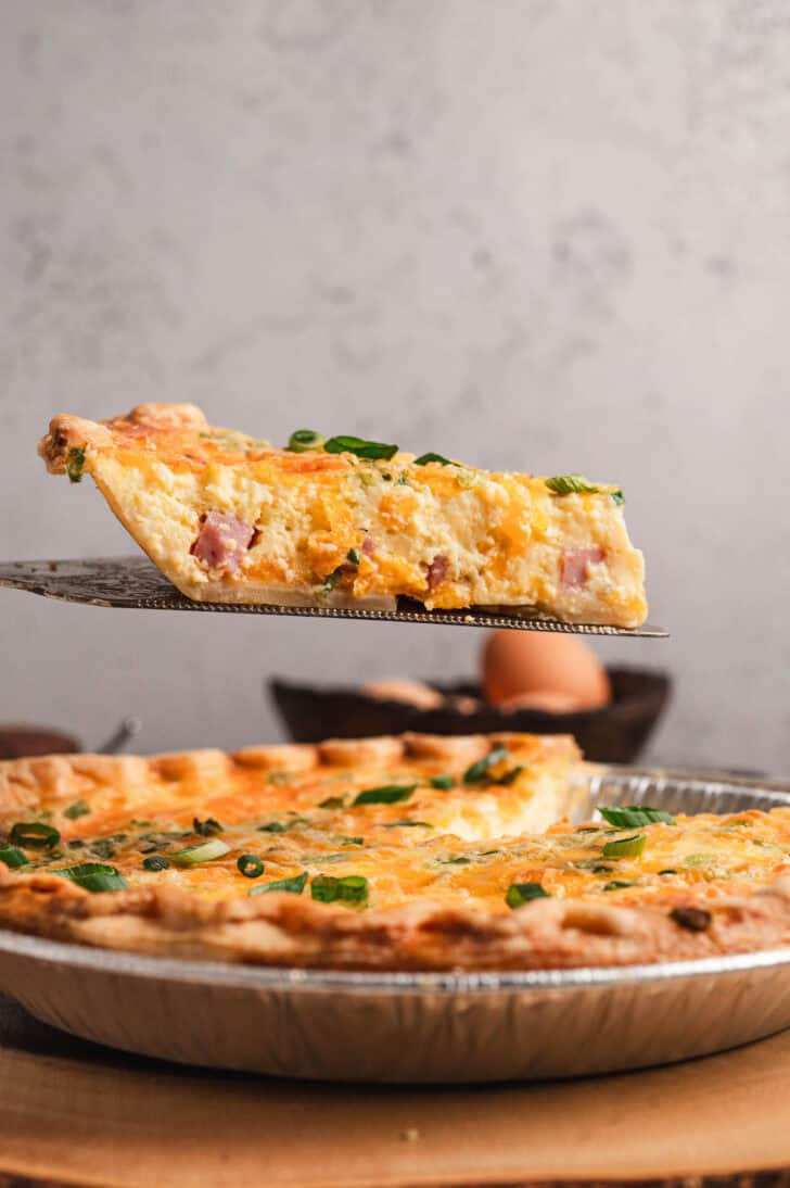 A slice of easy ham and cheese quiche being lifted from its pan.