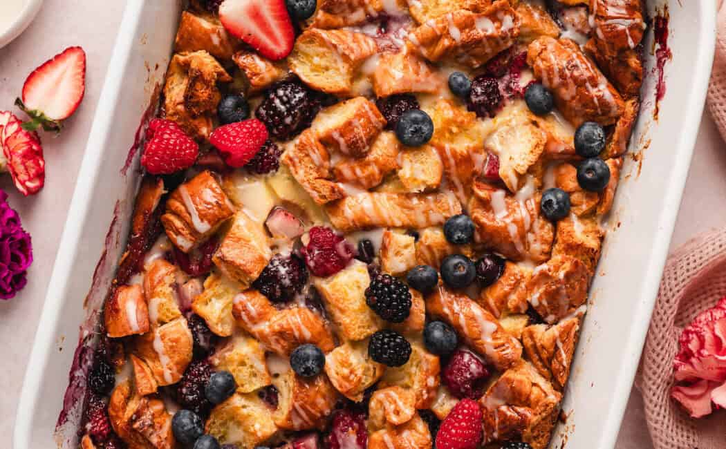 A white baking dish filled with croissant breakfast casserole with berries.