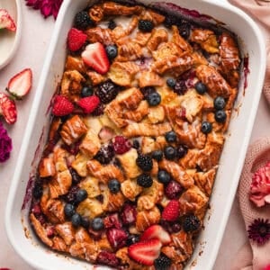 A white baking dish filled with croissant breakfast casserole with berries.