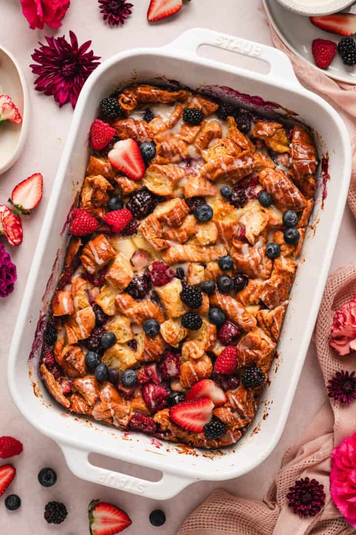 A white baking dish filled with croissant breakfast casserole with berries.