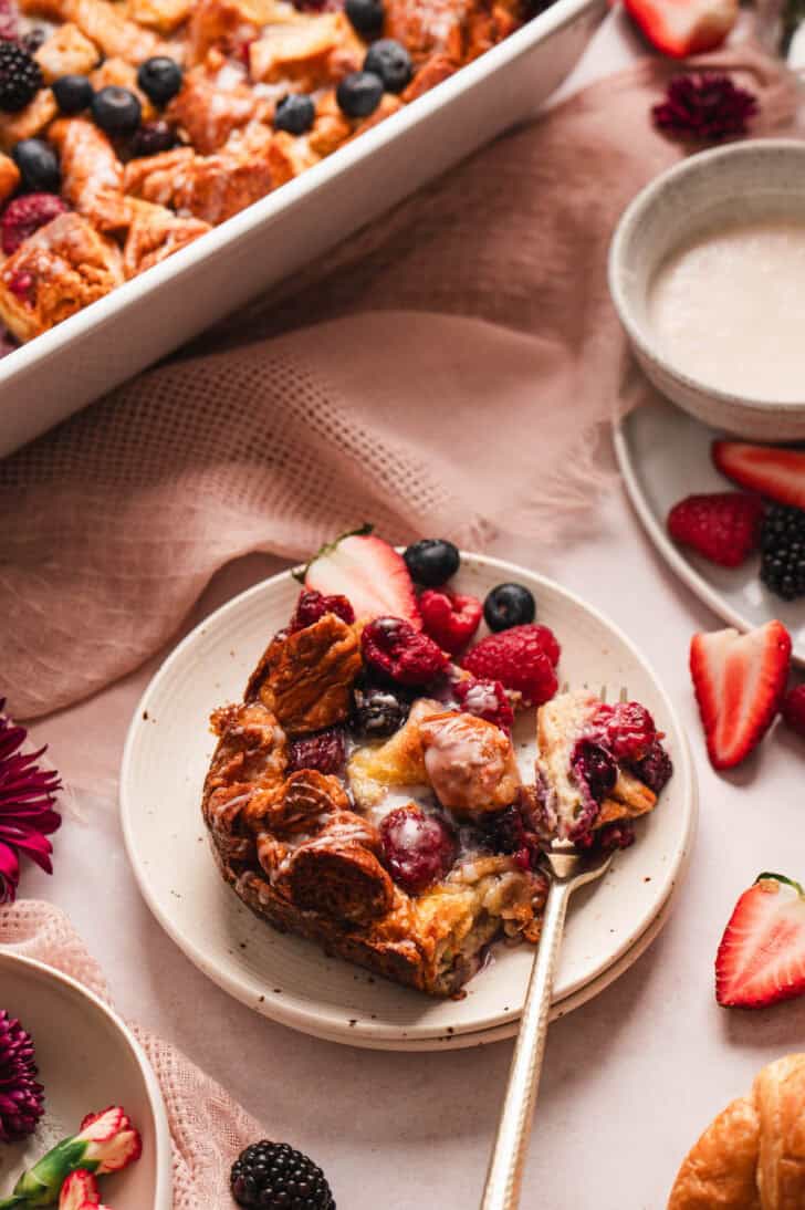 A fork skewering a bite of breakfast casserole sweet on a small plate.