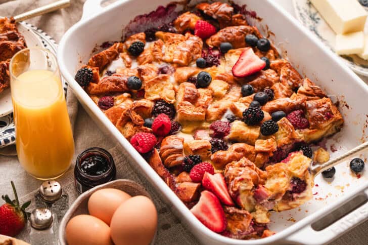 A white baking dish filled with croissant casserole in a brunch tablescape.