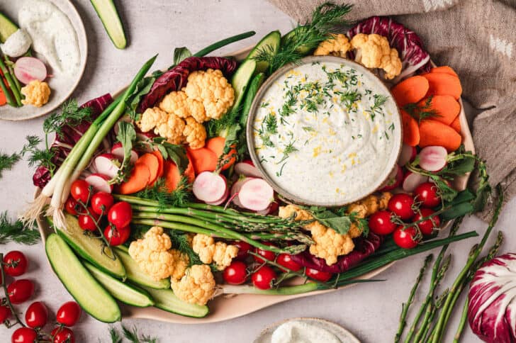 A platter filled with dill dip for veggies and colorful raw veggies for dipping.