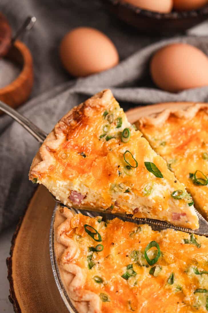 A slice of ham quiche being lifted from its pan.