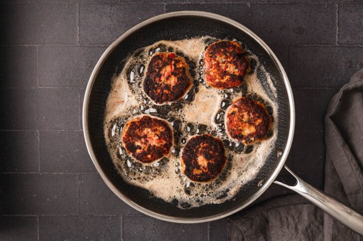 A recipe for salmon cakes being pan fried in a black skillet.