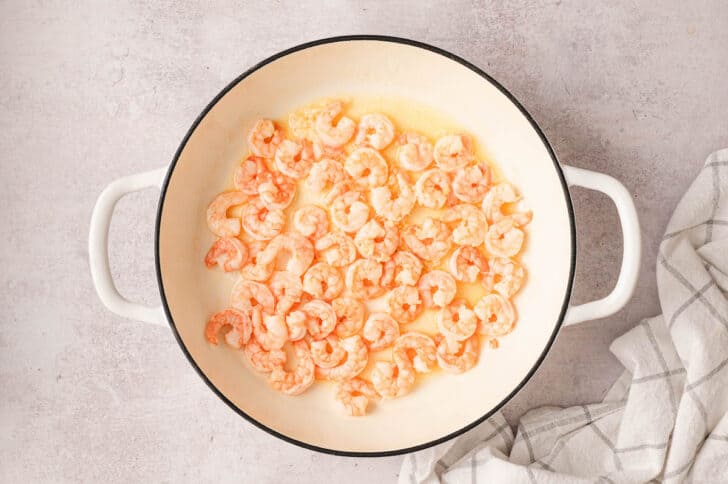 A white skillet filled with cooked prawns.