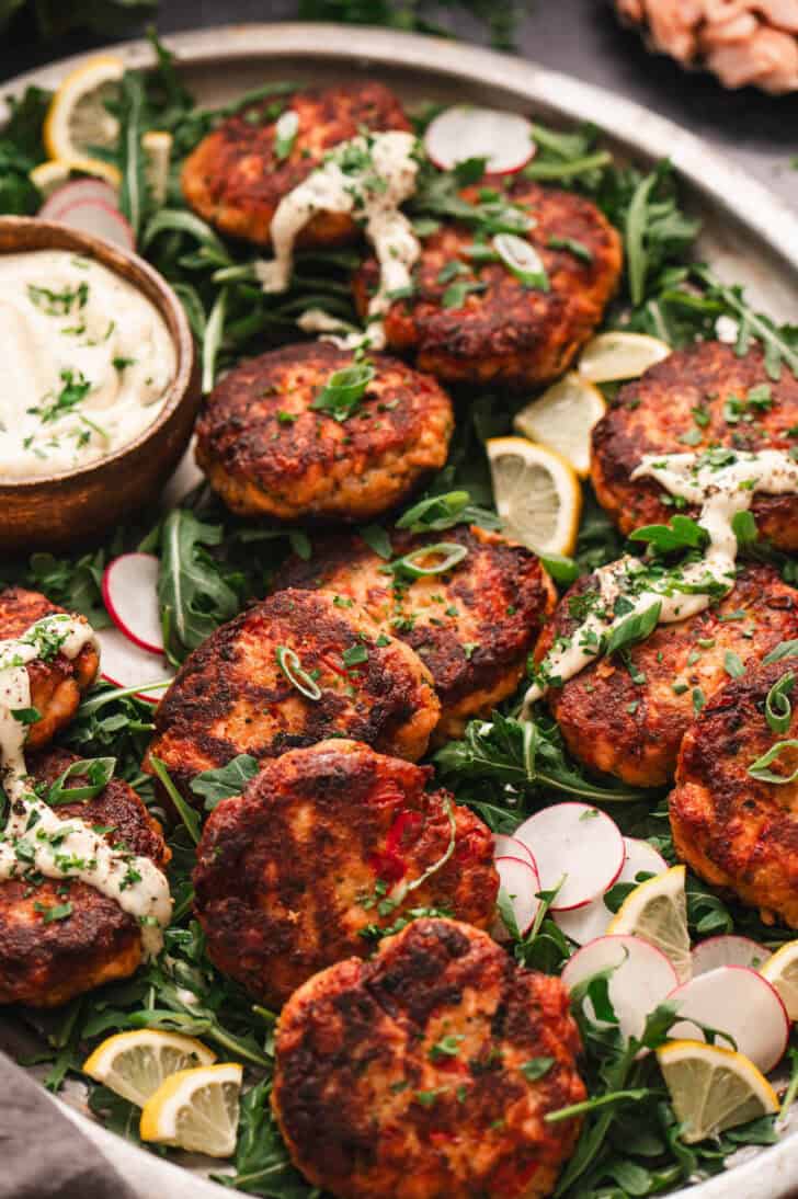 A large platter filled with fresh salmon cakes drizzled with creamy sauce.