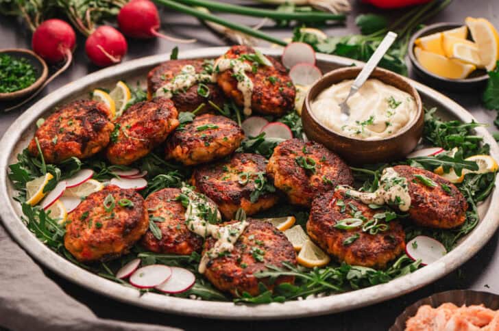 A large platter filled with salmon cakes from fresh salmon drizzled with creamy sauce.