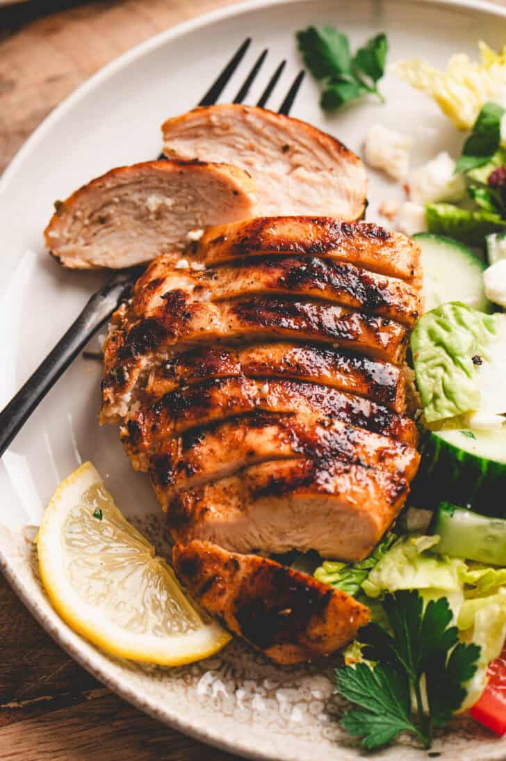 A chicken breast that has been marinated in an easy Greek chicken marinade, sliced, on a plate with salad.