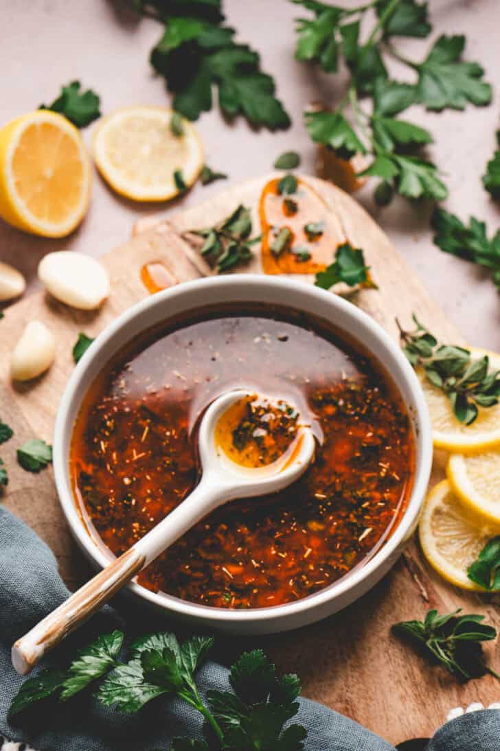 A bowl of lemon Greek chicken marinade with a white spoon in it.
