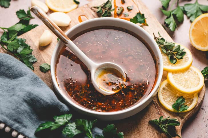 A bowl of Greek lemon chicken marinade with a white spoon in it.