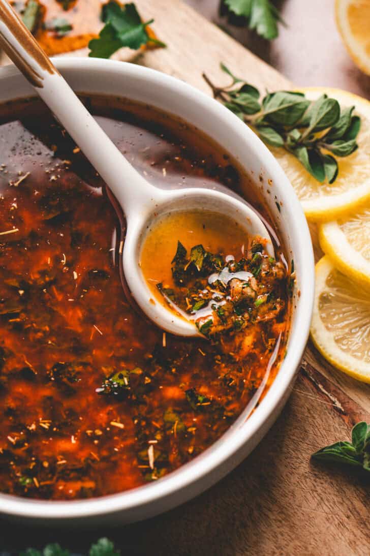 A bowl of the best Greek chicken marinade with a white spoon in it.