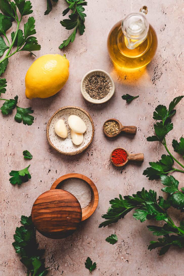 Ingredients on a textured surface, including herbs, spices, lemon and garlic.