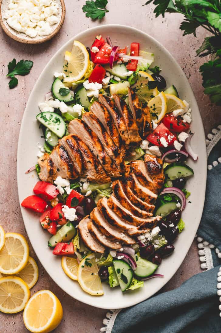 A salad with grilled chicken that has been marinated in Greek lemon marinade for chicken over it.