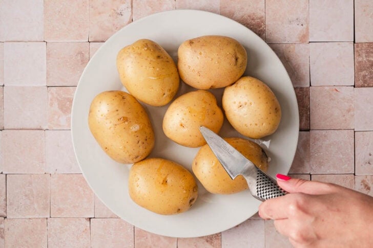 A hand piercing a plate of potatoes with a paring knife.