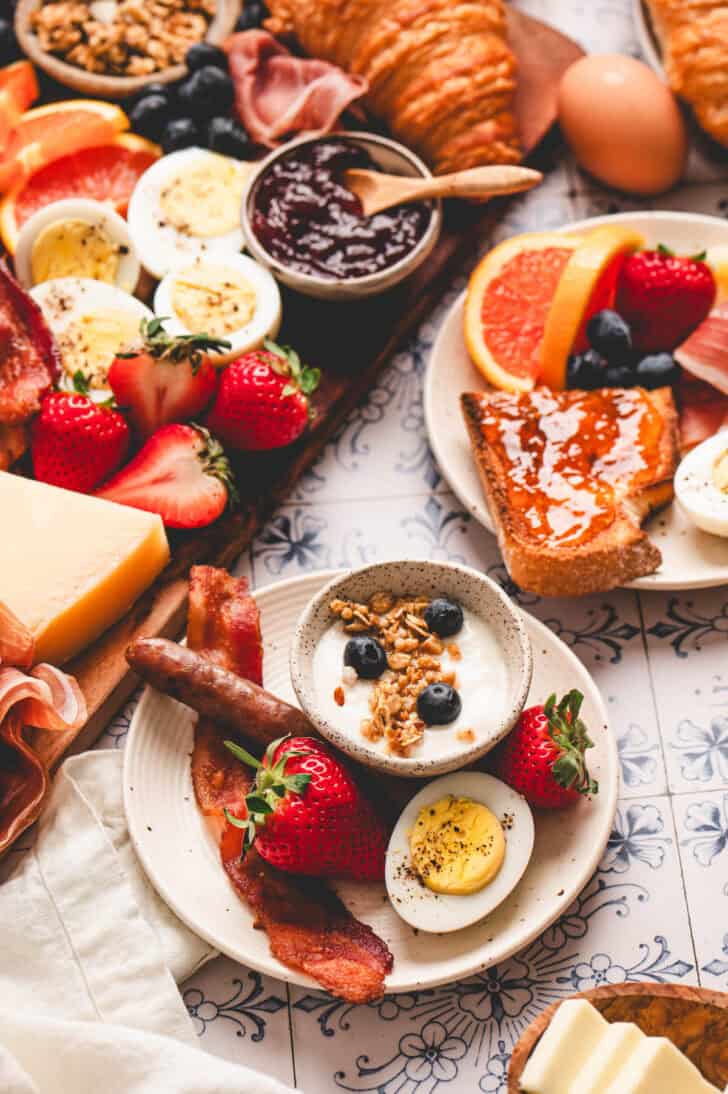 A plate with a serving of breakfast charcuterie board ideas, including yogurt, fruit, meat and a hard boiled egg.