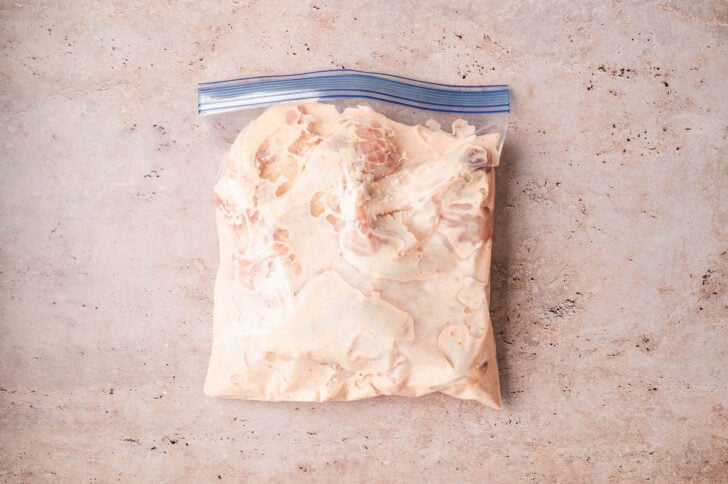 A zip top bag filled with raw poultry and a creamy sauce.
