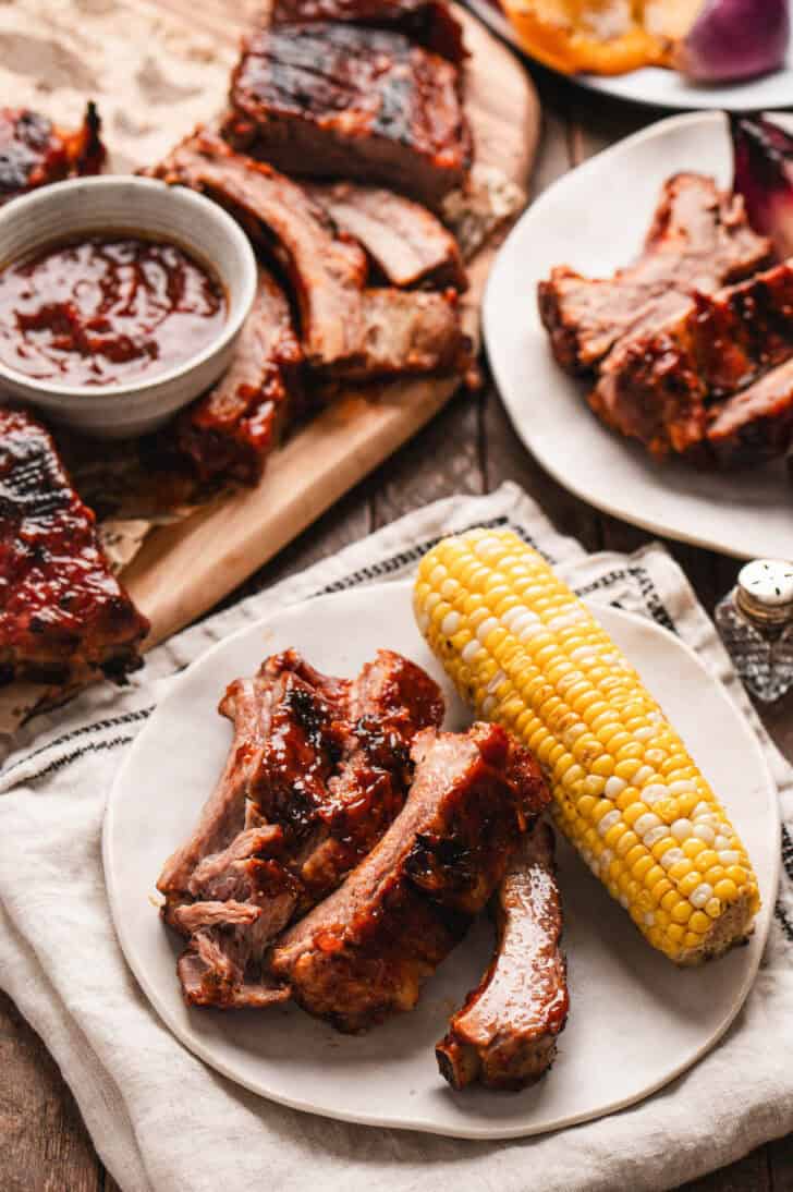 A white plate with root beer ribs and a piece of corn on the dob.
