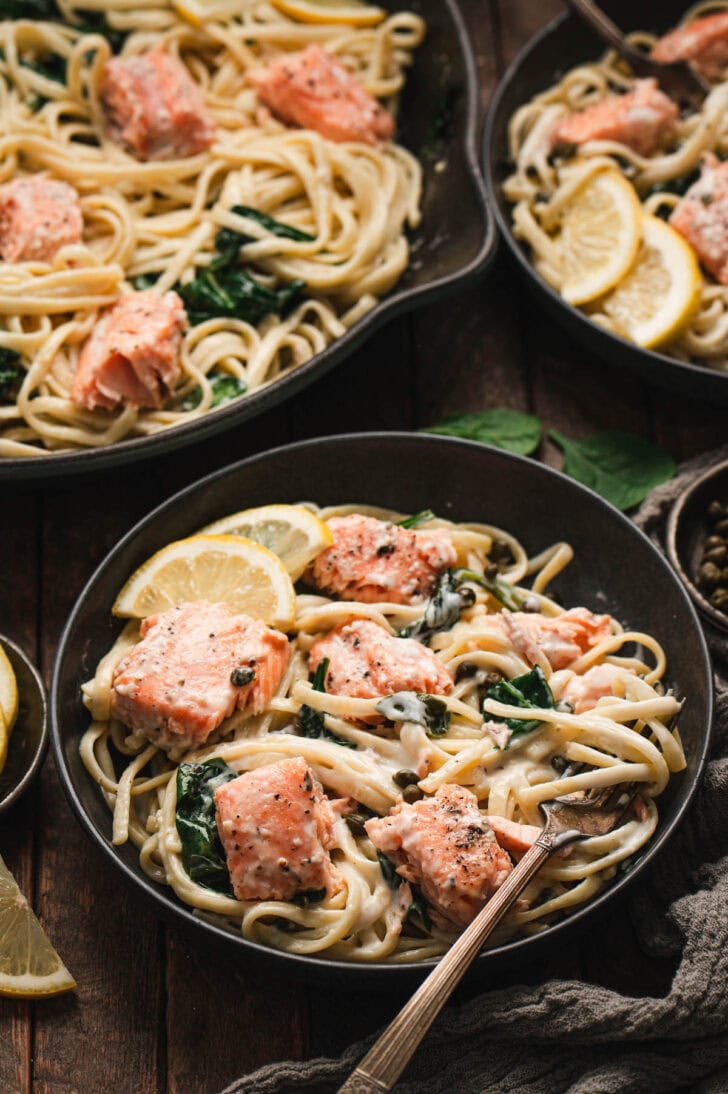 A black bowl filled with pasta and salmon.