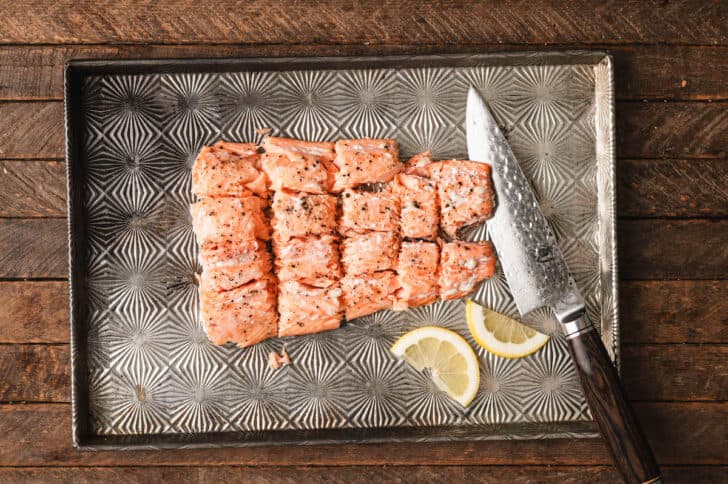 A piece of orange-hued fish on a baking pan that has been cut into large cubes.