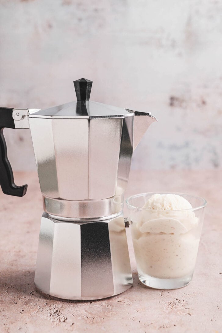 A moka pot next to a small dish of vanilla ice cream.