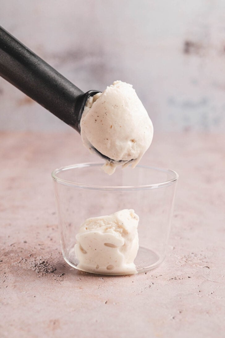 An ice cream scoop putting vanilla gelato in a small glass.