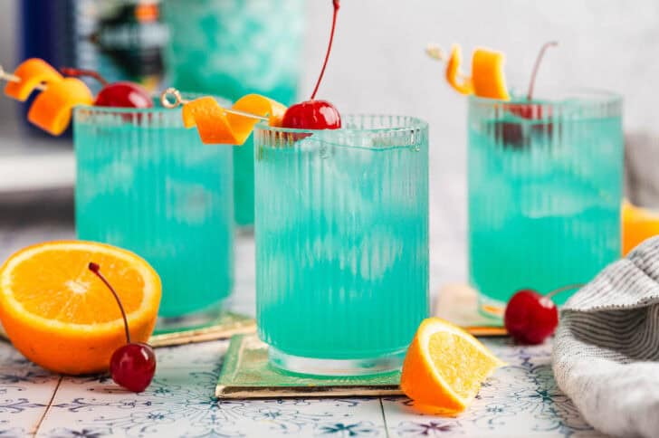 Blue colored mix drinks garnished with orange peels and cherries.