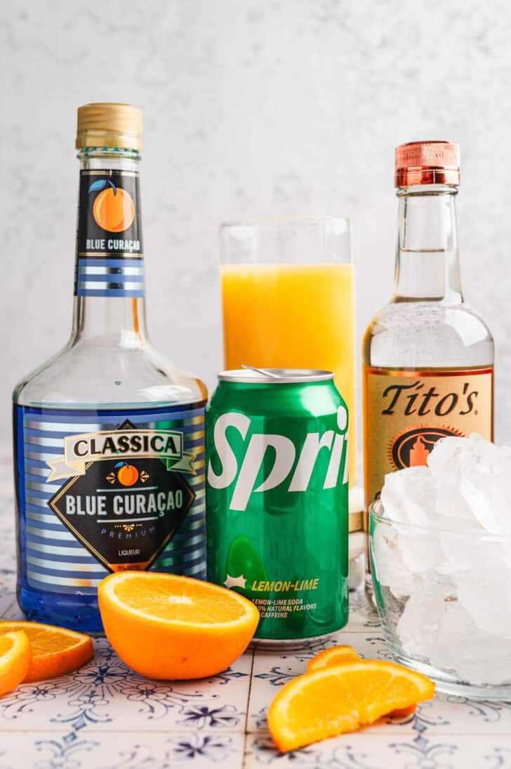 Ingredients in front of a light background, including curacao, sprite, vodka and orange juice.