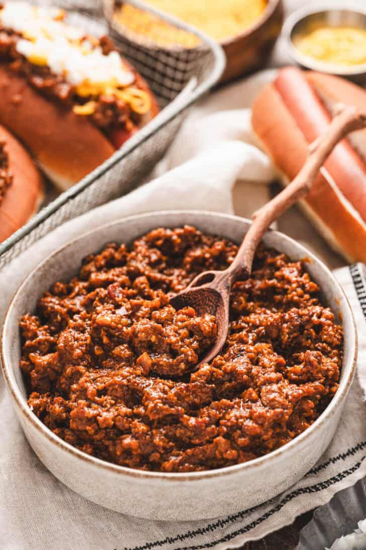 A wooden spoon in a bowl of chili recipe for hot dogs.