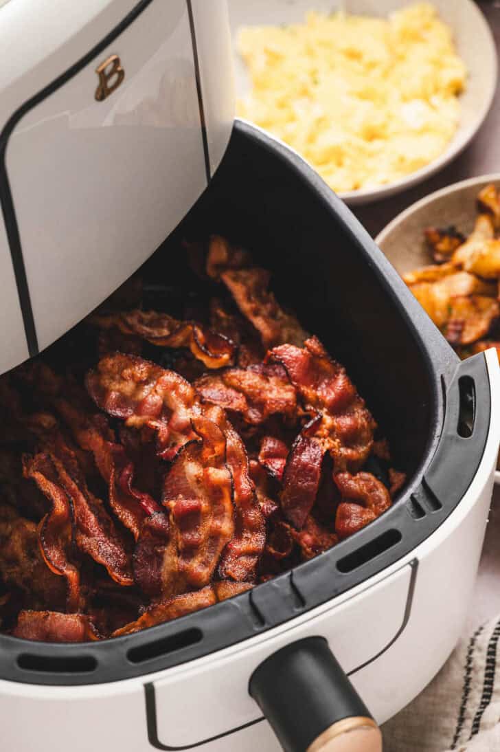 Bacon in air fryer with breakfast foods in the background.