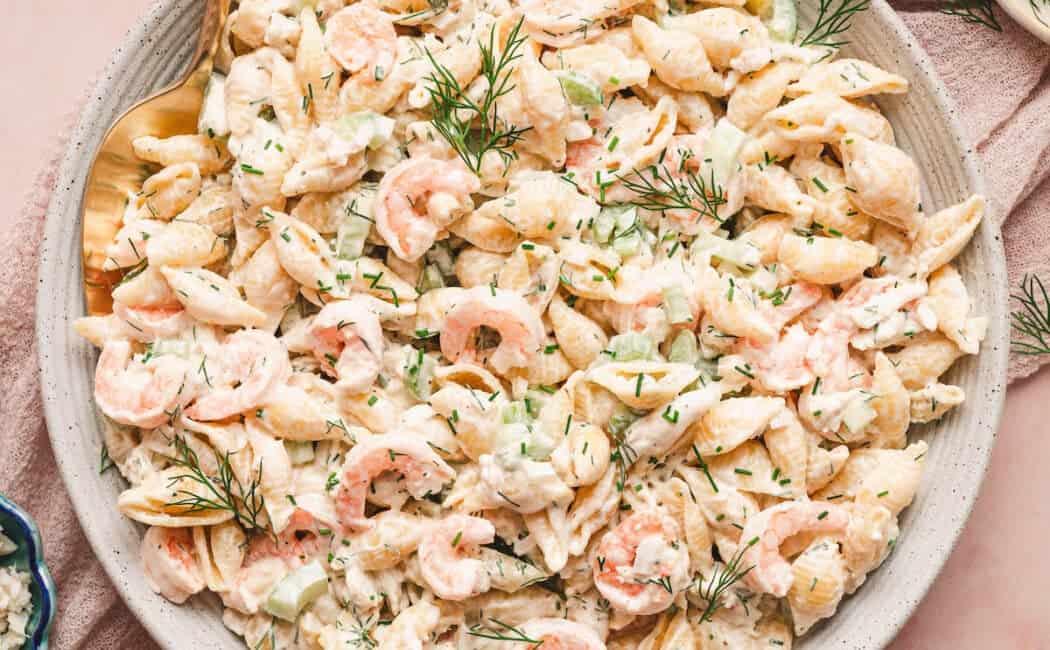 A bowl of seafood pasta salad on a pink surface.
