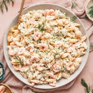 A bowl of seafood pasta salad on a pink surface.