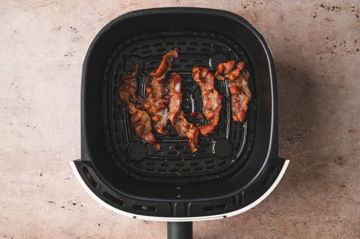 Cooked bacon in air fryer basket.