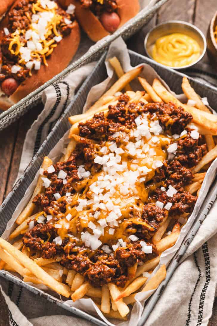 A pan with french fries covered in hot dog chili, cheese and onions.