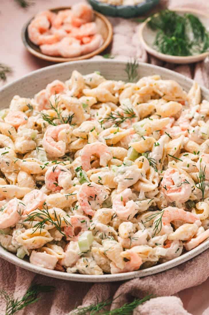 A bowl of seafood pasta salad with garnishes in the background.