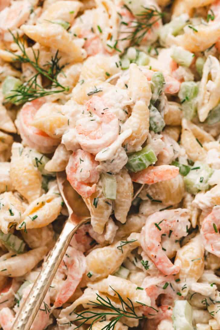 A closeup of a spoon lifting a scoop of shrimp crab pasta salad.