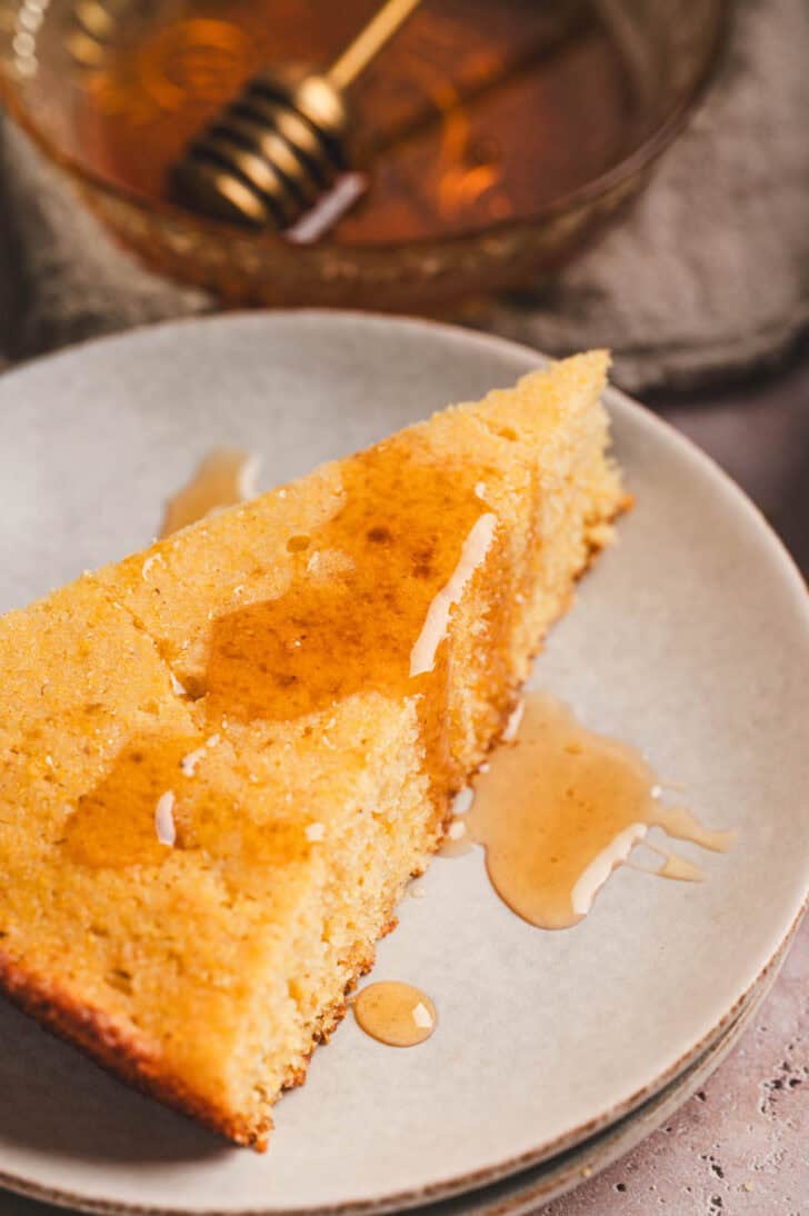 A slice of a honey butter cornbread recipe drizzled with honey on a small plate.