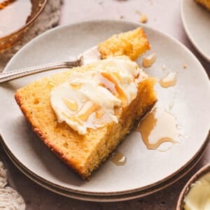 A slice of honey cornbread topped with butter and honey on a small white plate.