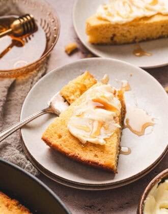 A slice of honey cornbread topped with butter and honey on a small white plate.