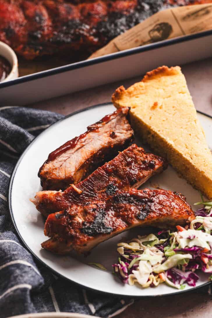 A plate with a serving of an Instant Pot ribs recipe, as well as cornbread an coleslaw.