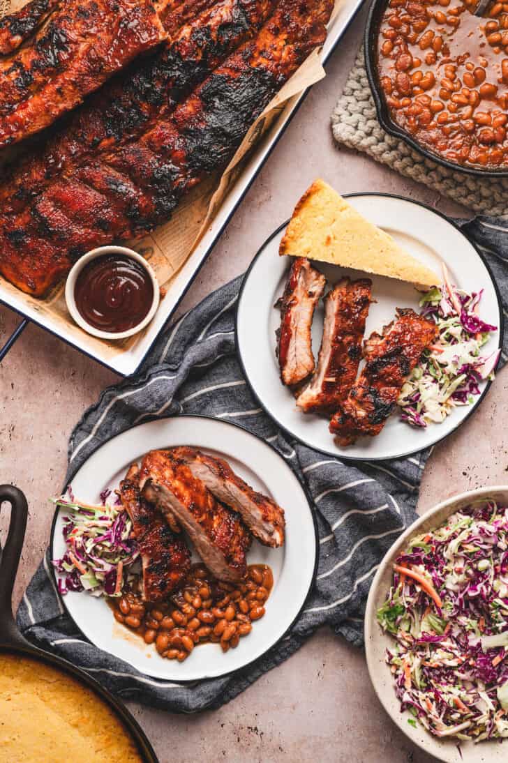 Plates filled with baby back ribs and side dishes for ribs like corn and slaw.