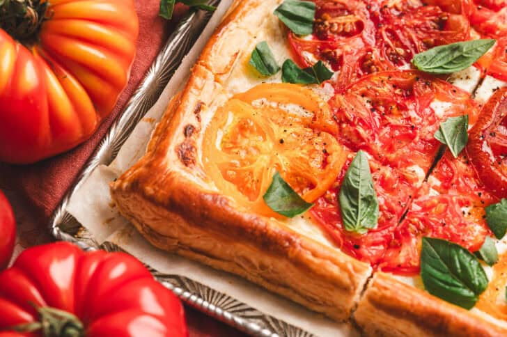 A corner of a tomato puff pastry tart on a baking pan.