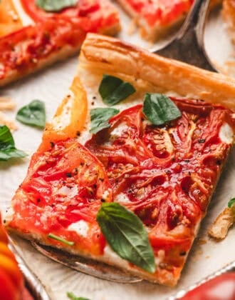 A slice of tomato tart with puff pastry on a serving utensil.
