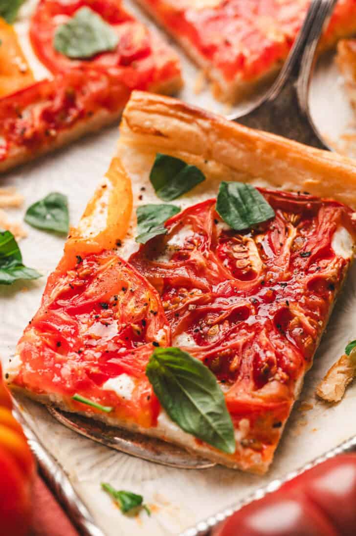 A slice of tomato tart with puff pastry on a serving utensil.