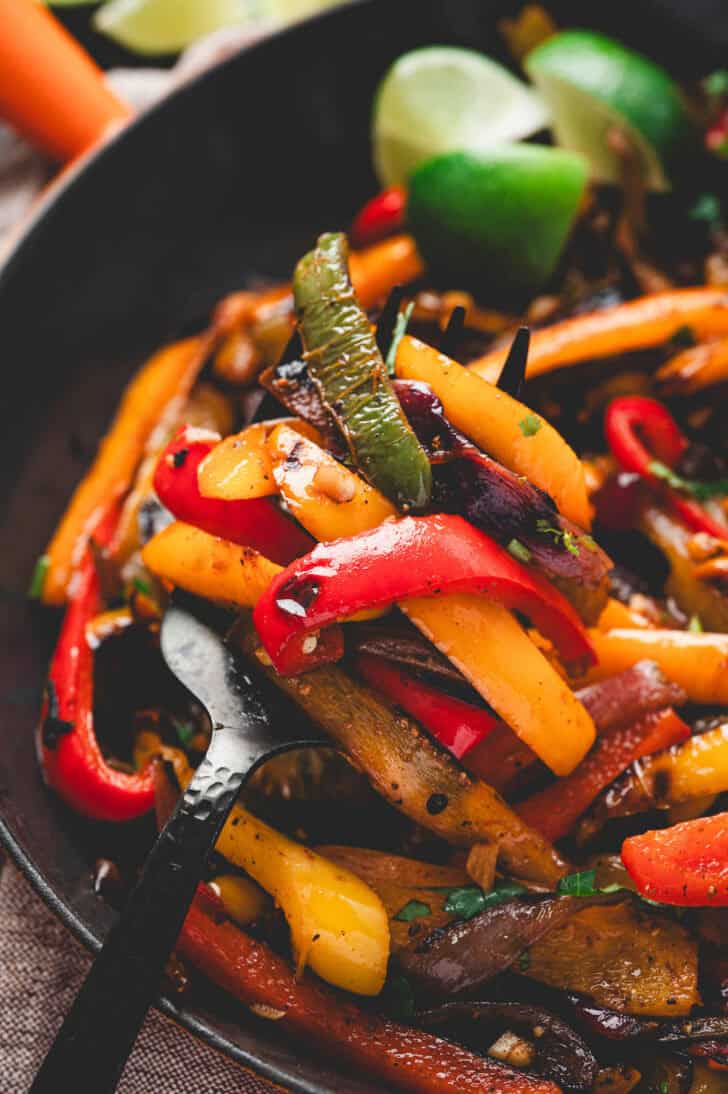 A spoon lifting a scoop of a fajita veggies recipe from a skillet.